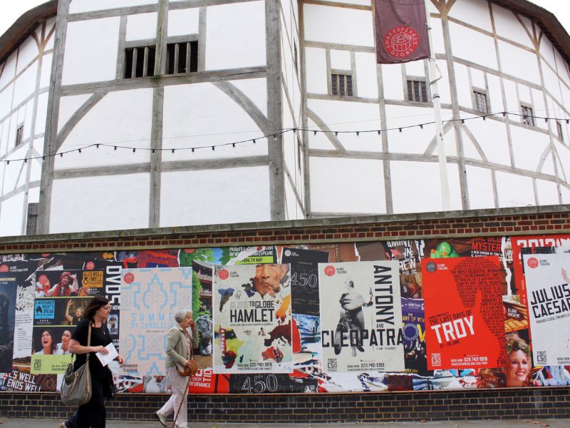 Passanten vor Plakaten mit Hinweisen auf Theateraufführungen am Globe Theatre