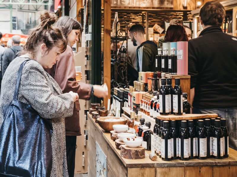 Passanten vor einem Olivenöl-Stand des Londoner Lebensmittelmarkts